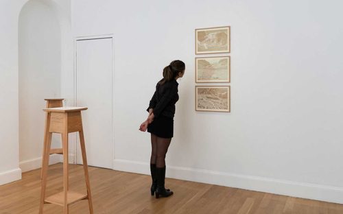 A woman leans in to look at three sepia-toned photos of glaciers.