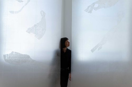 Portrait photo of artist Sarah Casey, standing between and behind two of her large, paper-based works.