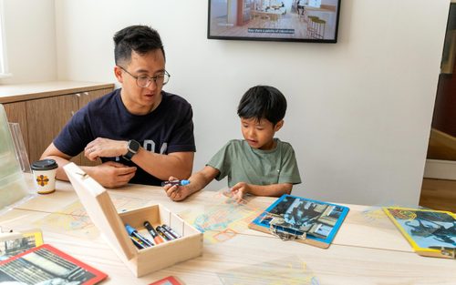 A father sits at a table with his son which he draws on an acetate sheet
