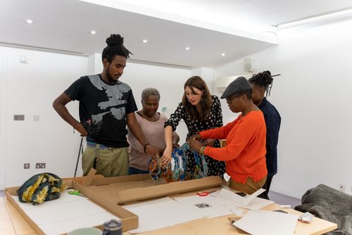 Five people are working together to construct a sculpture made of colourful glass rings, which get progressively larger from one end of the sculpture to the other.