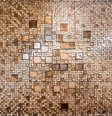 A wall covered in brown and cream tiles of varying size and hue.