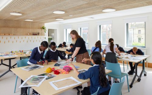 A school group sat around four tables, working on a creative project involving photos of sculpture, transparent sheeting and brightly coloured string.