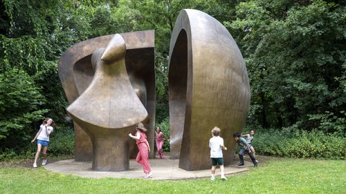 A group of six children, of mixed ages, playing hide and seek in and around a huge bronze sculpture.