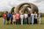 Eleven people of varying ages stood together outdoors in a line. They are in front of a large bronze sculpture by Henry Moore.