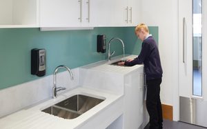 A boy washing his hands at one of two dual-height sinks.